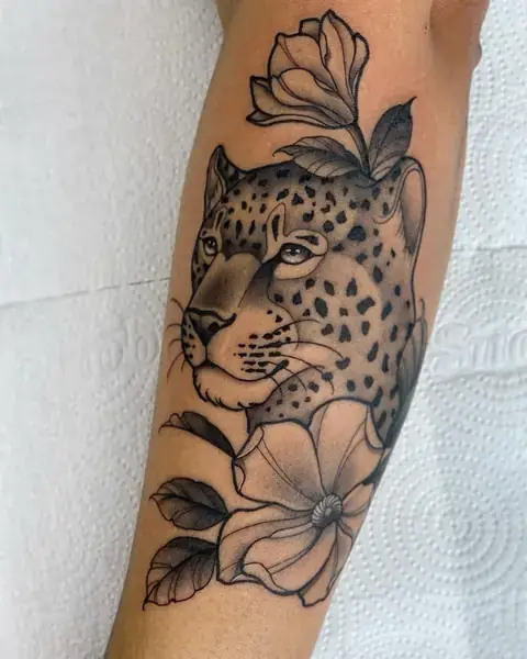 Tatuagem neotradicional de onça com flores no antebraço