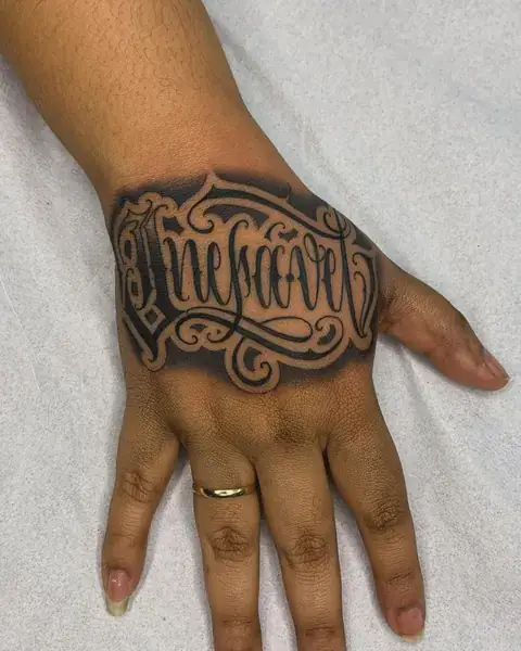 Custom lettering “Inefável” tatuado no dorso da mão