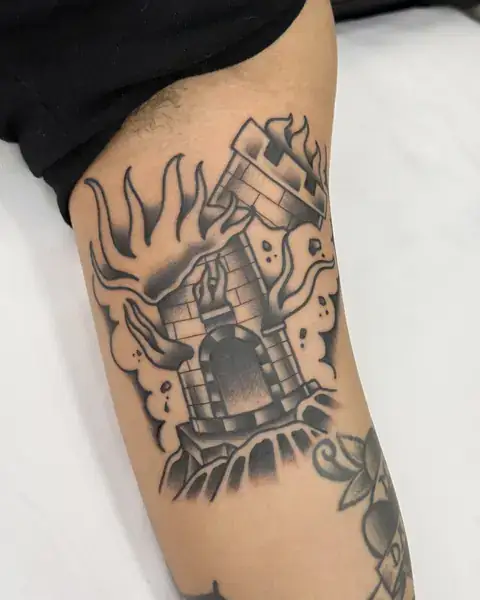 Tatuagem old school de torre em chamas no braço